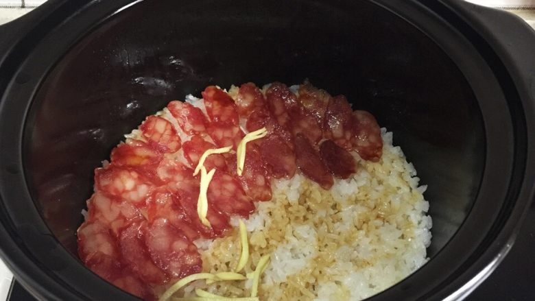 腊肠煲仔饭,锅里开了转小火,铺上腊肠片焖两三分钟开盖浇上酱汁,放上姜丝。