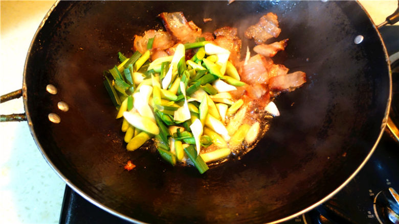 蒜苗炒腊肉,将蒜苗头子放入锅里,翻炒。
