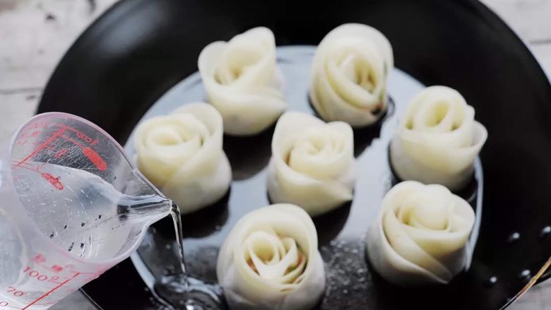 玫瑰花饺子, 煎花饺(完全就是煎饺的做法)。锅底抹上一层油,把花朵们放进去,再倒入100毫升的水,盖上锅盖。大火烧1分钟,转小火煎2分钟;看到锅底的水烧干了,淋点油进去;再小火焖1分钟。关火,用铲子铲出来,装盘。