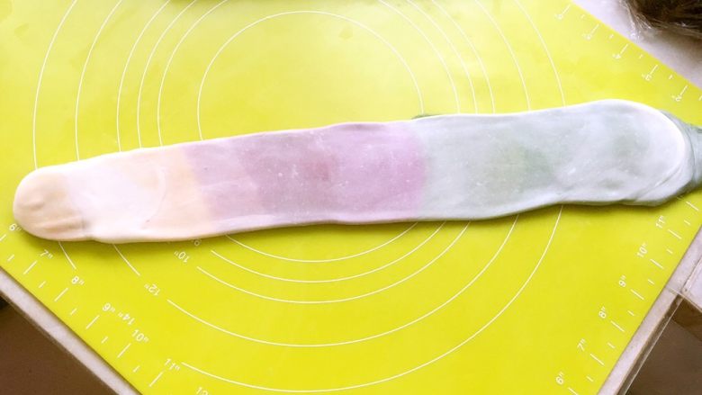 彩虹蛋黄酥,将松弛好的面团按照长条排列的方向,再次擀成长条,之后从浅色处开始卷起来