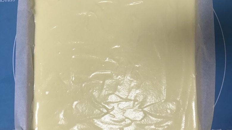 美味蓝莓酱棉花蛋糕,烤箱预热140度5分钟,将蛋糕糊倒入烤盘中,用刮板刮平。