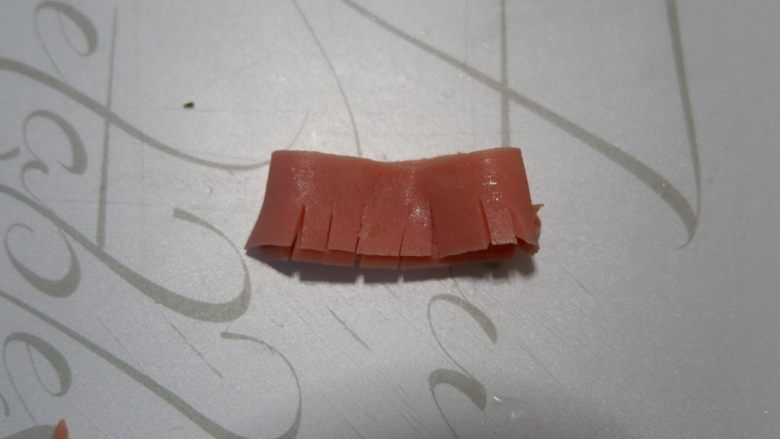 卡通小熊萝卜糕便当盒「14」,将火腿肠折叠起来,用到切出条纹,不要切断。