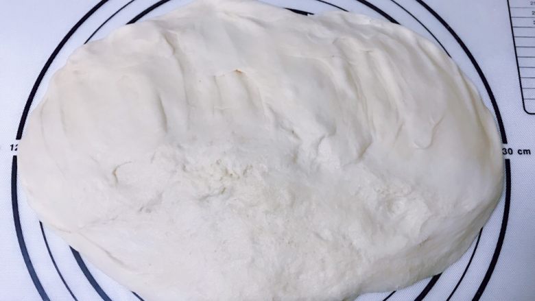 爆浆肉松面包,案板上撒少许干粉,手沾少许干粉,取出发酵好的面团轻拍排气