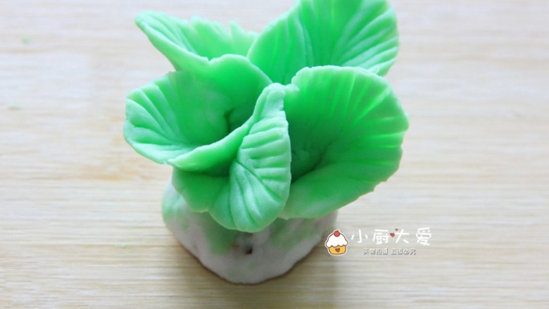 过年菜---福瑞白菜,依次把所有叶子都压好。取其中一片叶子,底部再捏大一点点。把捏好的叶子往身前粘过来,然后顺同一方向把5个叶子都粘好。捏好后,对白菜的底部进行整形,并且把叶子整理好,这样,一个白菜生胚就做好了。