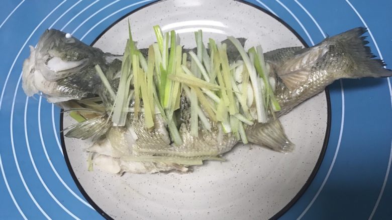清蒸鲈鱼,在鱼身上面铺上葱丝和姜丝。