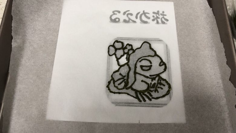 旅行青蛙蛋糕卷,把打印好的镜像的旅行青蛙图案上放上一张油纸,用最深色的抹茶黄油霜勾勒出轮廓