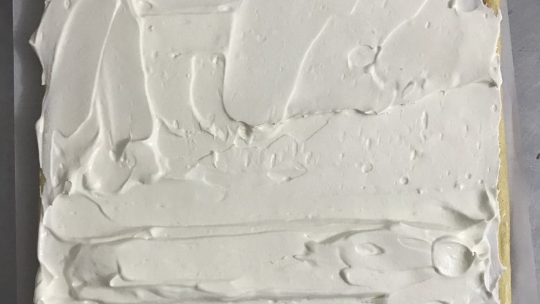 爱心草莓蛋糕卷,蛋糕片下垫上一张较大的油纸,将奶油抹在蛋糕片上,靠近身边的蛋糕卷用奶油堆一个小山丘。