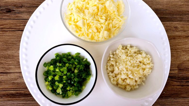 蒜蓉芝士焗阿根廷红虾,虾在腌制的过程,我们来准备调料,蒜去皮切蒜末,葱洗净切葱花,芝士用刀剁碎一些
