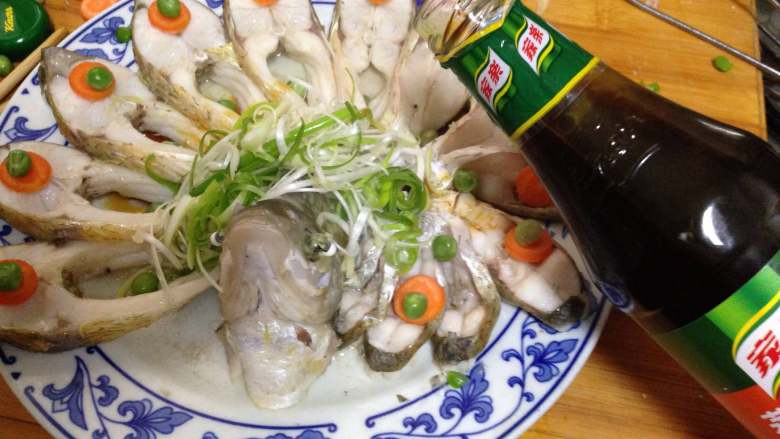 年味——宴客大菜孔雀开屏鱼,
鱼出锅后,倒掉盘子中蒸出的水,摆上泡好的葱丝,用青豆做装饰倒上<a style='color:red;display:inline-block;' href='/shicai/ 864'>蒸鱼豉油</a>