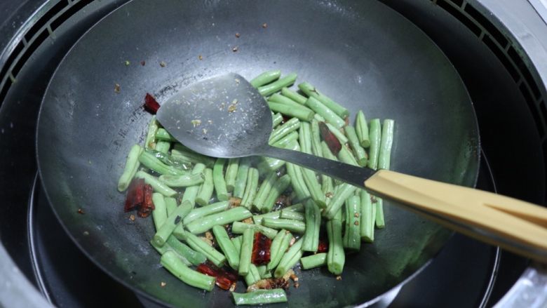 干煸四季豆,按图中这样，用锅铲压一压，可以将四季豆表面炒得微微焦，但要控制好火候。