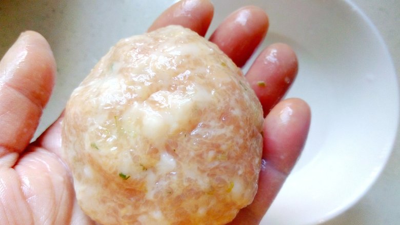 年味~蟹粉狮子头,将拌好的肉分成几份,两手蘸生粉水后,逐份放在手掌中,用双手来回翻动,交替接着肉圆,滚成表面光滑。