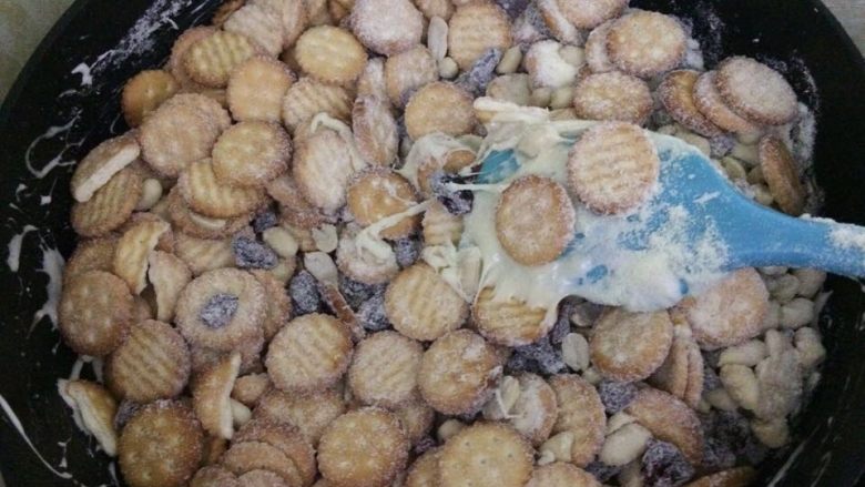 网红雪花酥,倒入混合的饼干和坚果、蔓越莓干,也是快速的翻拌混合均匀。