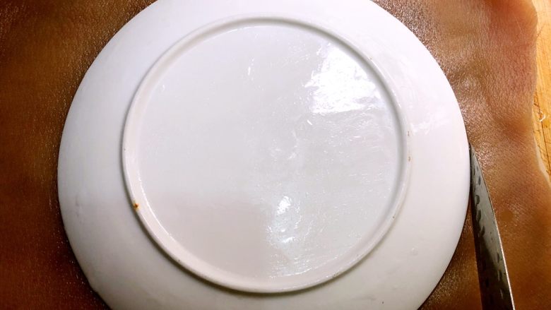 青田蹄膀,肉皮弄干净以后沥干水,肉皮朝上铺在案板上,盖上一个8寸的碗,用刀沿着碗边割一圈
