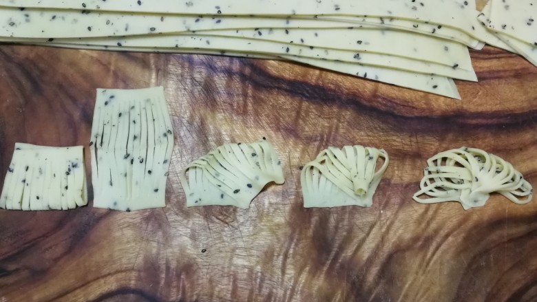 年味~花式炸麻叶,这是4指宽面片做成扇形的整形方法,把4指宽面片对折后切成10~12股,展开后左上角对右下角按紧,然后右上角也慢慢收拢与右下角右侧部分重合按紧,最后左下角也慢慢收拢与右下角左侧部分重合按紧,稍微整理一下就成为扇子一样了