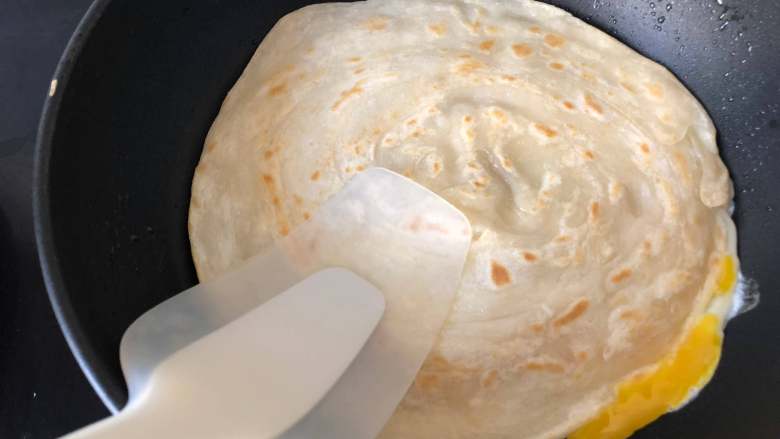网红手抓饼,翻面时打入一个鸡蛋,用铲子轻压手抓饼,使鸡蛋和饼粘在一起