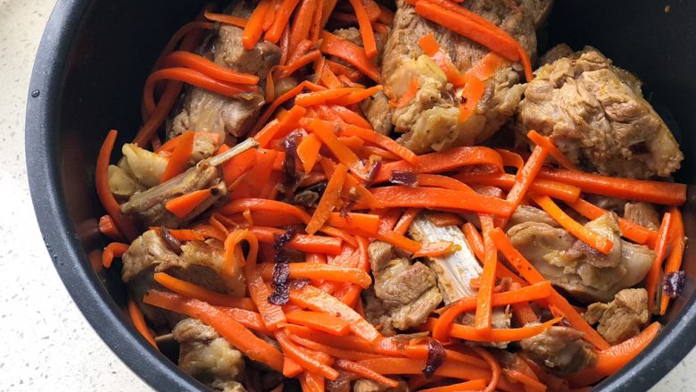 新疆抓饭,把炒好的胡萝卜羊排倒入电饭煲内胆里;