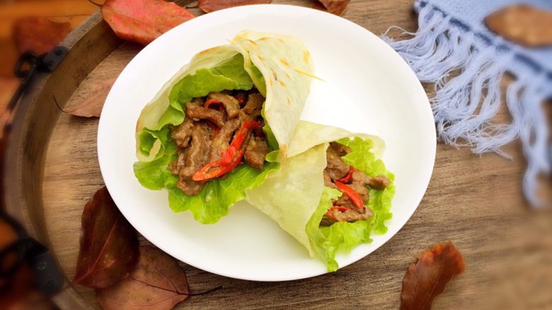 嫩牛肉卷饼,放入炒好的牛肉条,再将饼周围的边缘折起卷起,用牙签固定住即可食用。