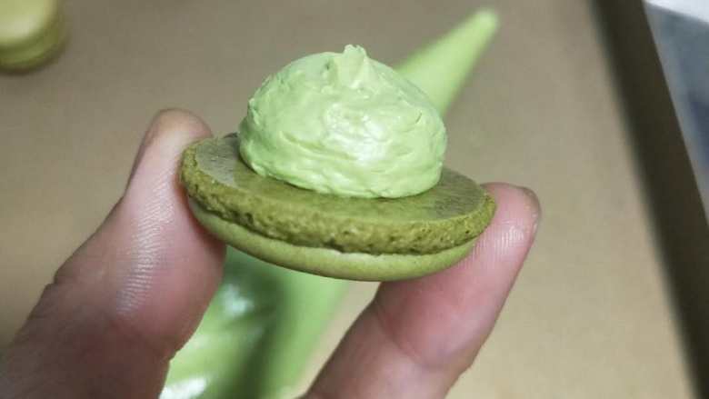意式抹茶马卡龙(无色素版),将内馅装入裱花袋。可以用裱花嘴也可以不用装圆形裱花咀,我是没有装的。取一个马卡龙外壳如图挤上抹茶内陷,再盖上一个大小相同的。
