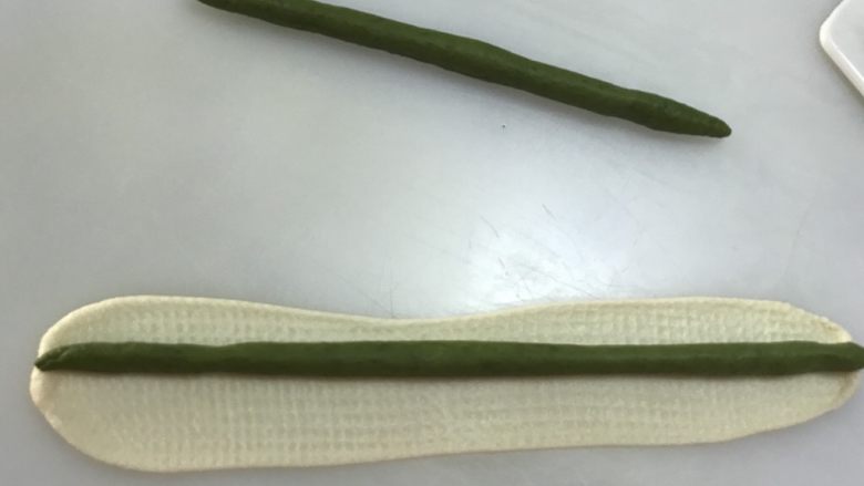玫瑰花吐司,分别取3个12克的绿色面团搓长成棒状,再分别取3个12克的白色面团擀开擀长,把绿色面团包住,捏紧收口处。