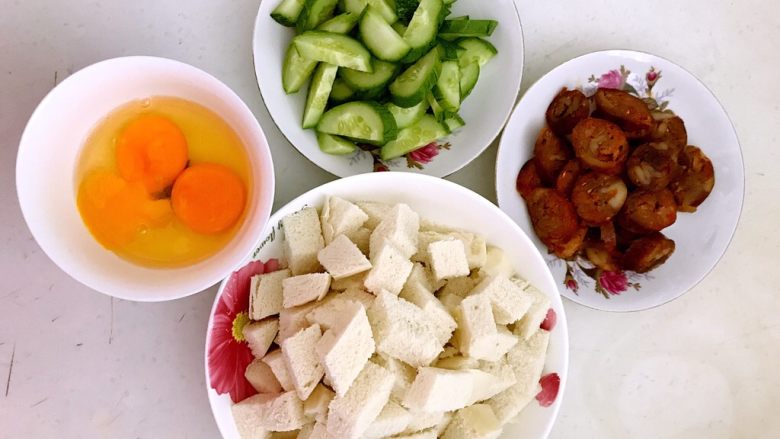 剩馒头的春天 腊肠炒馒头,鸡蛋打入碗里,馒头切成1.2㎝见方的小丁,腊肠切成小片,黄瓜切成稍厚一点的小片