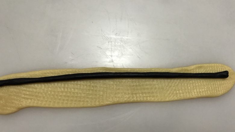 罂粟花吐司,将黑色面团搓成约15厘米的棒状,黄色面团擀压成15*3厘米的面皮,包入黑色棒状面团,即完成花朵的中心。