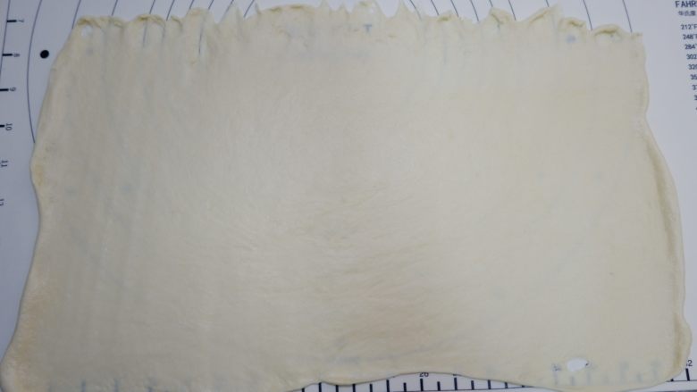 椰蓉蔓越莓花环面包,用擀面杖把面团擀成50×35cm的长方形,上边缘压薄,,可以借助刮刀均匀摊平, 注意尺寸,不要差太多,不然做出的花环可能会小。