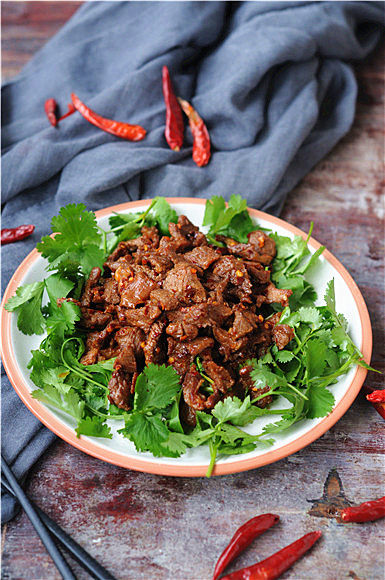孜然羊肉,出锅前加入辣椒碎,炒好的羊肉盛入铺满香菜的盘中就可以上桌了