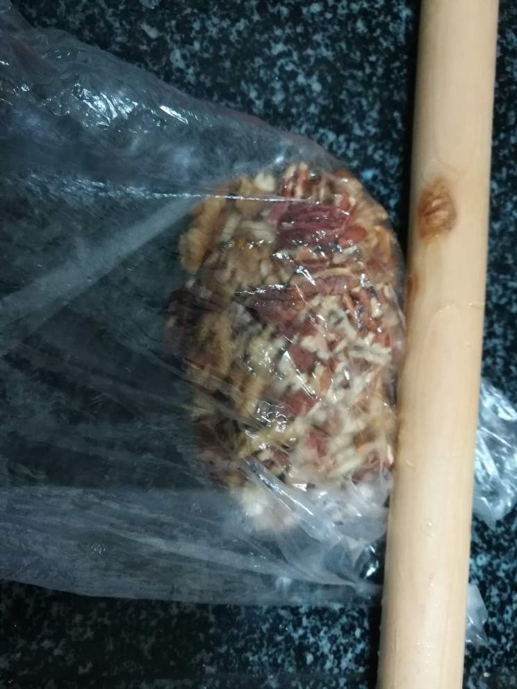 香蕉芝麻坚果仁馅饼,把碧根果仁和核桃仁放在保鲜袋里,用擀面杖擀成碎。