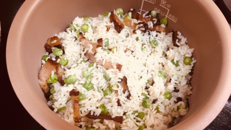 豌豆腊肉饭,铁锅关火,炒过的腊肉豌豆米放进电饭煲(如果用铁锅继续,需要加水,然后小火焖熟米饭,期间需要不断转锅,不是翻炒,是转动锅,均匀受热。饭好了锅底会有锅巴,不糊的话也能吃。比较麻烦需要一直转动,因为还要用锅炒菜所以我直接用电饭煲。)