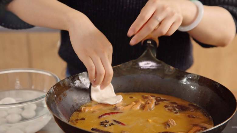 地锅鸡【曼食慢语】,将小面球拿出来按扁,再用手直接扯成椭圆形的饼,然后贴在锅边,让饼一半贴在锅边一半飘在汤上