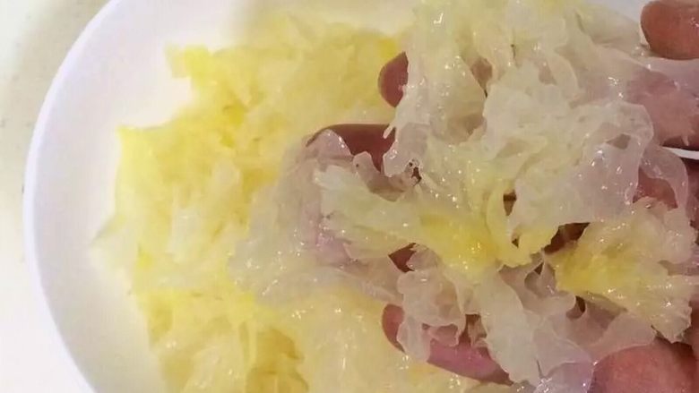 牛奶桃胶银耳羹,把银耳的根部去掉,照着它的纹理把它撕成片条状。