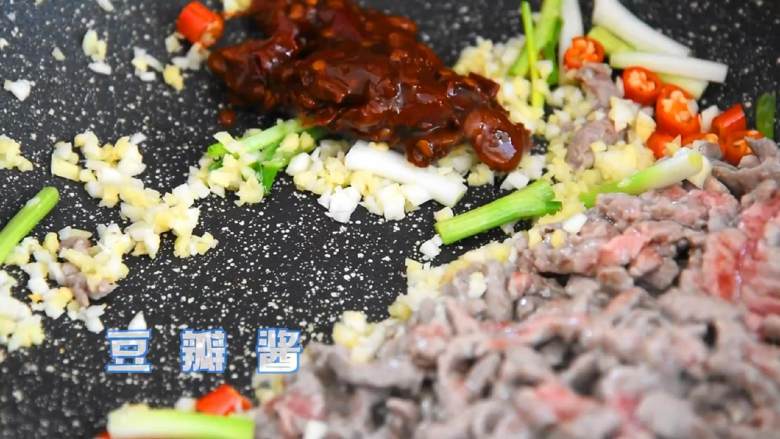 芹菜牛肉,变色的牛肉丝推至锅中的另一边,空出来的地方倒入葱白、小米椒、姜蒜末,一起炒香后再加入豆瓣酱和肉丝炒至上色。