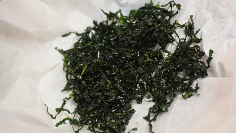 菠菜松（佐粥小菜）,炸到卷起，颜色变深就捞起，放入铺了油纸的碗中，继续下第二撮菠菜丝，就这样一撮一撮地来，直到全部炸完捞起关火。