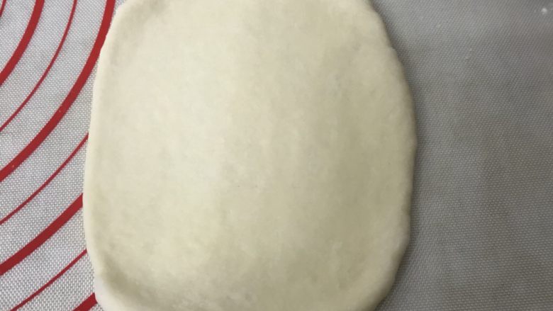 奶香糯米排包,取一个松弛好的面团光滑面朝上用擀面杖擀成长舌形状,边上的气泡用手拍打掉