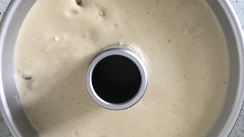 红枣戚风蛋糕,打蛋盆离中空模具20厘米高倒入18厘米中空模具中,这一步的目的是为了把个别大气泡拉抻破掉,两个大拇指按住中空柱大力振几下模具,把大气泡震出来。