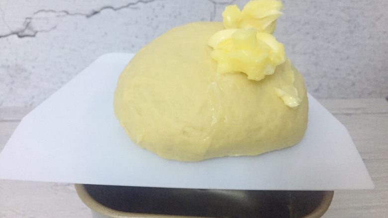辣肉松面包卷,扩展阶段即面团可拉出厚膜时,加入黄油,继续和面揉至完全阶段。此时面团可以拉出薄且不易破的膜。