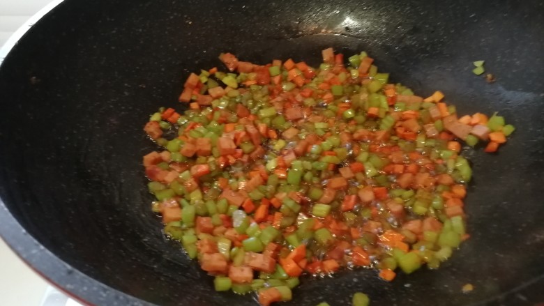 黄油版&黄金火腿蛋炒饭,把芹菜丁,胡萝卜丁和火腿丁放进锅里翻炒。