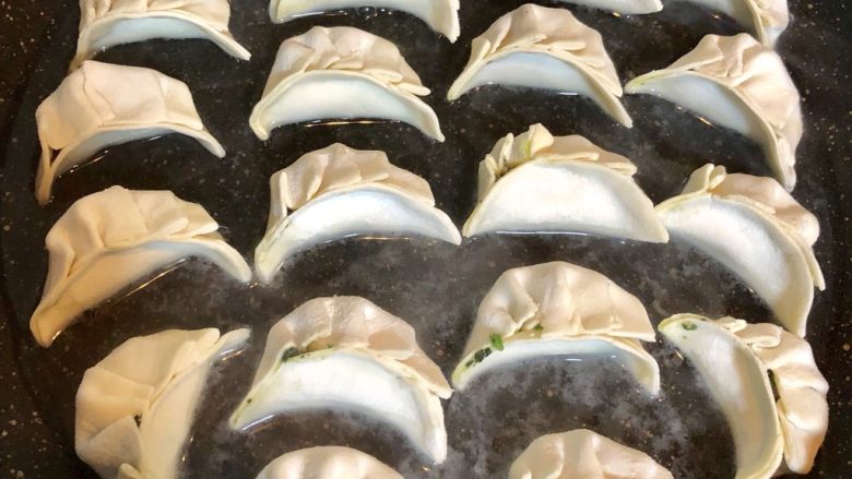 蛋抱饺子,饺子放入不粘平底锅中排列均匀,倒入约饺子三分之一的水和少量油。盖上锅盖最小火煮至锅底只有少量的水。