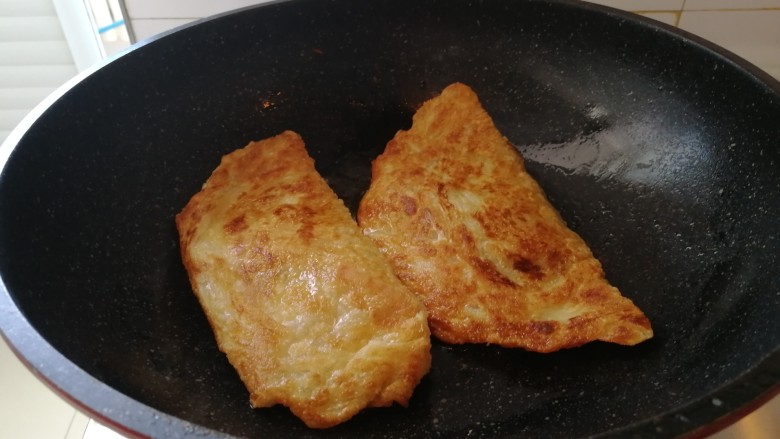 快手早餐&芹菜火腿手抓饼,起油锅,油热开始烙饼,烙至两面金黄色就好了(如图),从中间切开,摆盘。