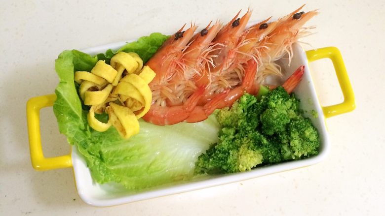 鲜虾时蔬饭团便当,在便当盒或着碗内铺上一张洗净的生菜叶,把煮好的虾依次摆好,西兰花和鸡蛋花朵也放上。