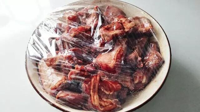 无锡排骨,准备大碗放入排骨,淋入料汁,充分拌匀。用手抓捏让排骨把料汁都吸收干净,然后用保鲜膜密封放入冰箱腌制2个小时。
