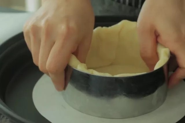 流心芝士挞,饼干面团擀至2-5mm的厚度,裁成8寸圆形大小,填入4寸慕斯圈模中,尽量把折角的部分压实。