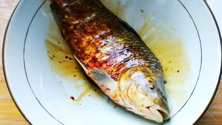 香煎鲫鱼,放进酱油、两滴麻油、些许食盐已混合均匀的腌料里,裹满鱼身。(腌制数分钟)