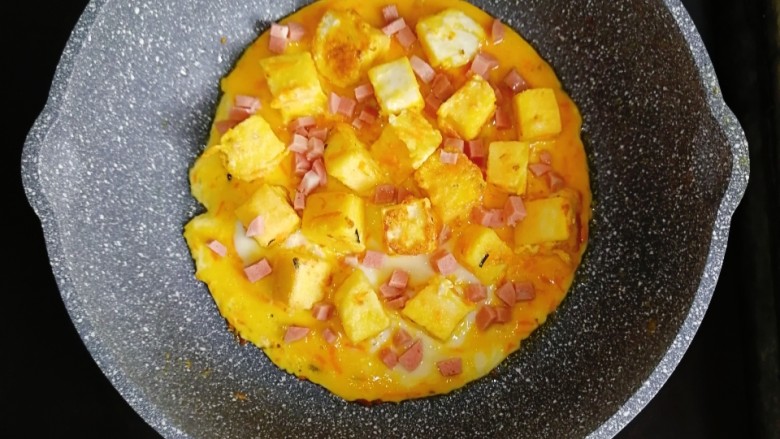 宝宝辅食—香肠馒头抱蛋,蛋液半凝固时,放入馒头块,撒上香肠,继续小火满煎