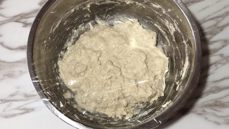 天然酵种橄榄菜欧包,盖上保鲜膜,让面团在室温发酵3小时。在30分钟、60分钟、90分钟、120分钟、150分钟时折叠面团,共五次。