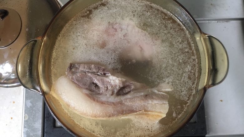 回锅肉,猪肉切成两大块,放入锅里加入适量水,水以淹过猪肉为宜,加入大火烧沸水,小火煮猪肉。