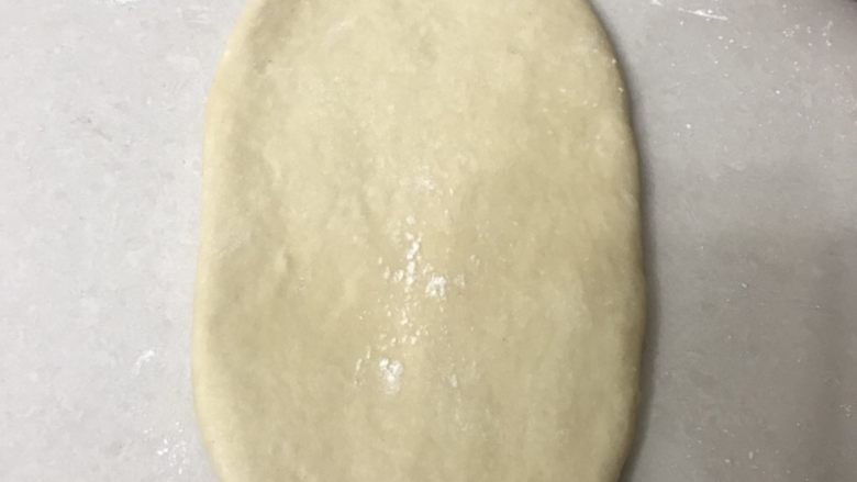 荷香茯茶奶茶吐司,取一个松弛好的面团,用擀面杖从中间向两头擀成长舌形,边上的气泡用手拍掉