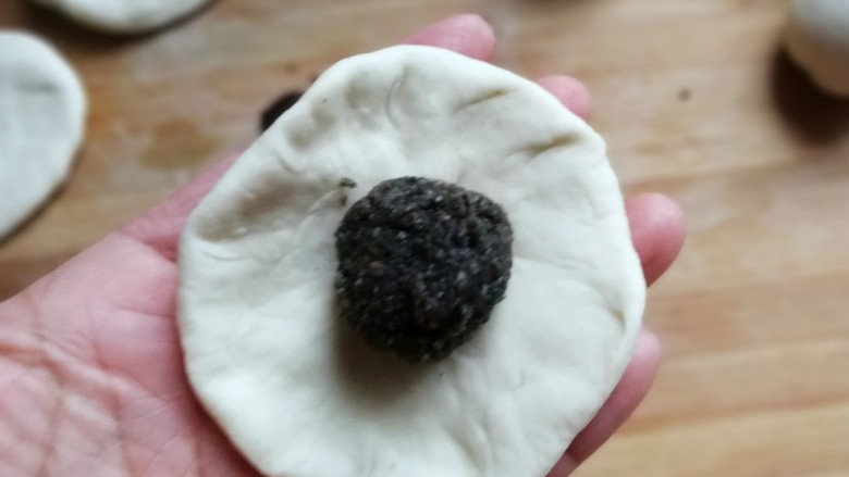 熊猫豆沙馒头,取一份醒发好的面团,用手压成中间厚四周薄的面片,再放上一份豆沙馅儿,包起来然后搓圆
