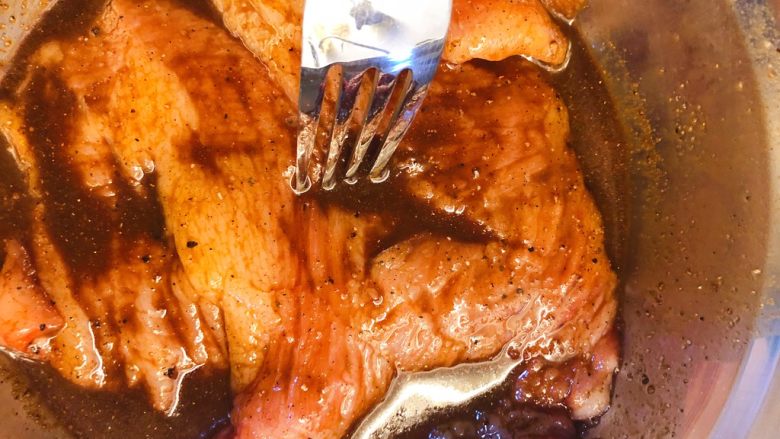炭烧猪颈肉,用叉子在肉厚的地方多插几个洞,让腌料渗入。