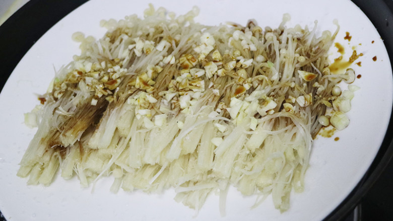肉末金针菇,锅中烧开水,金针菇放入盘中,撒上蒜末,撒上盐、糖、蒸鱼豉油、生抽,蒸5分钟。